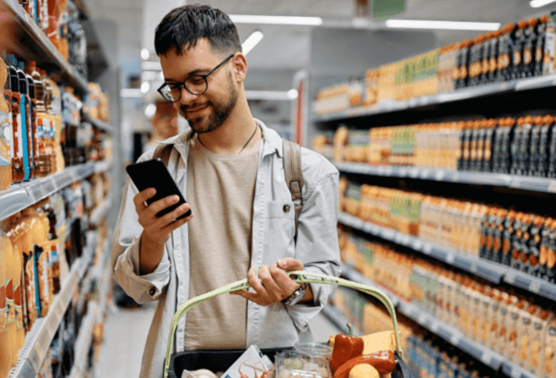 A shopper standing in a packed store aisle, looking at his phone for help finding what he wants